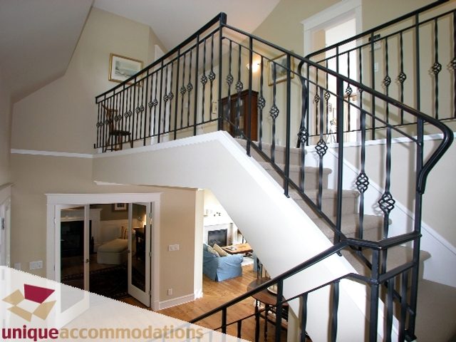 Staircase with ornate black railings and light wood flooring leads to upper levels in a spacious, well-lit house. - 3586 Creery Ave, West Vancouver