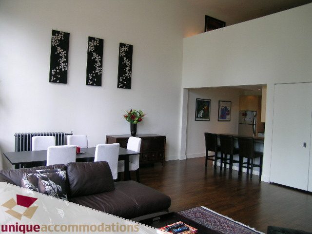 Bright living room with hardwood floors and modern decor, featuring a sofa, dining area, and kitchen counter.