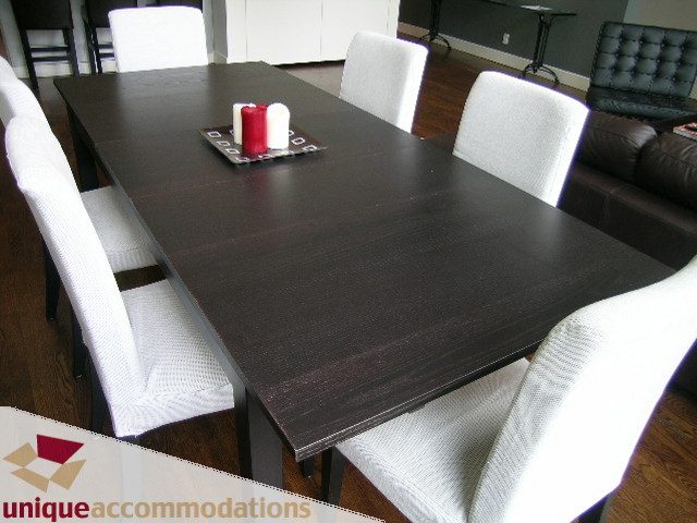 Dining area with dark wood table, white chairs, and red candle centerpiece. - PH2 - 869 Beatty Street, Vancouver Downtown
