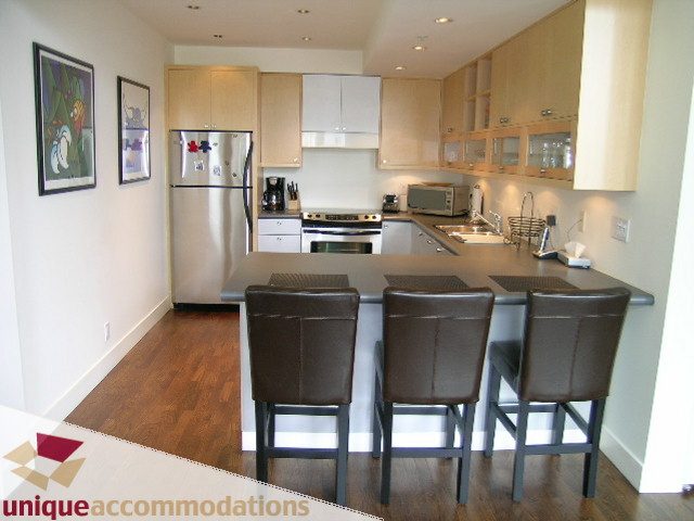 Bright kitchen with stainless steel appliances, dark leather bar stools, and hardwood floors. - PH2 - 869 Beatty Street, Vancouver Downtown