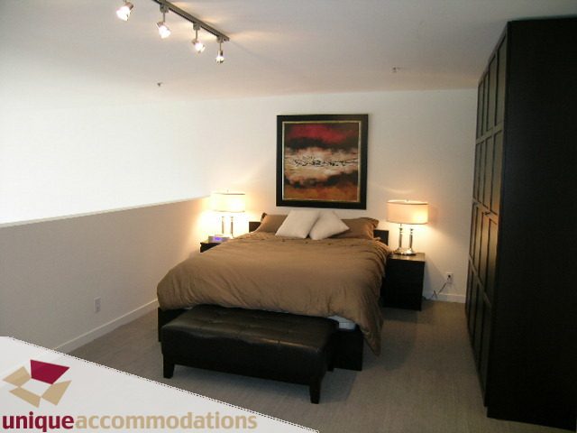Furnished 1-bedroom penthouse with modern decor, large bed, leather ottoman, and wall art. - PH2 - 869 Beatty Street, Vancouver Downtown