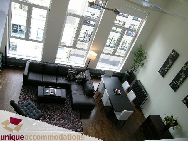 Bright living room with large windows, hardwood floors, and a cozy sofa setup. - PH2 - 869 Beatty Street, Vancouver Downtown