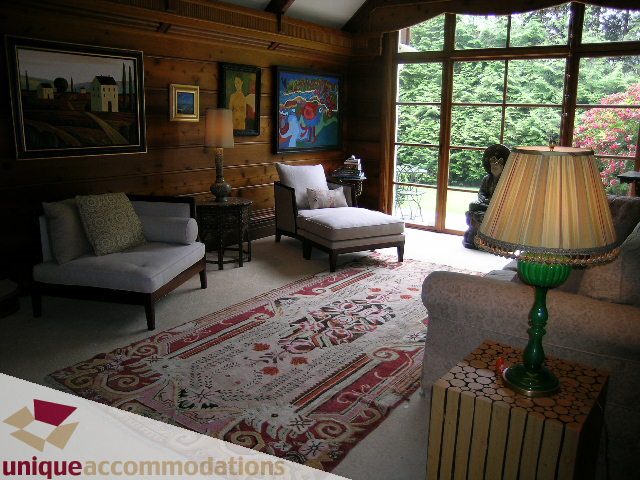 Cozy den with patterned rug, wooden furniture, and large windows showing greenery. - 419 Inglewood ave, West Vancouver