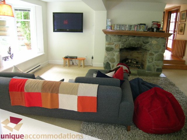 Furnished living room with stone fireplace, modern TV, and cozy seating. - 419 Inglewood ave, West Vancouver