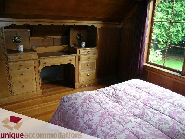 Furnished bedroom with wooden desk, patterned bedspread, hardwood floors, and a view of greenery outside. - 419 Inglewood ave, West Vancouver