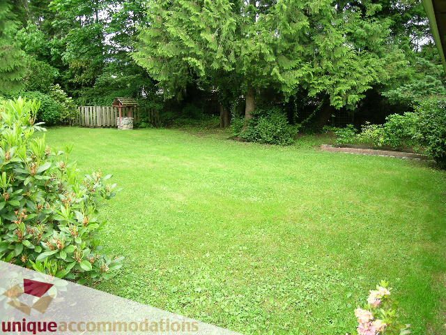 Spacious backyard with lush green grass and vibrant flowers. - 419 Inglewood ave, West Vancouver