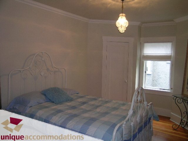 Bright bedroom with white iron bed frame, checkered bedding, and hardwood floors. - 1505 Grand Blvd., North Vancouver