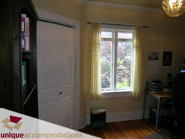 Bright living room with hardwood floors and a large window, featuring a desk and bookshelf. - 1505 Grand Blvd., North Vancouver