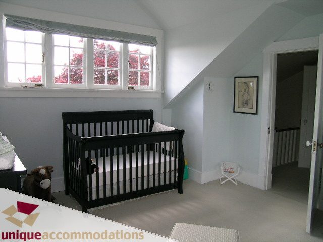 Bright nursery with black cribs, white walls, and large windows showing red trees outside. - 1505 Grand Blvd., North Vancouver