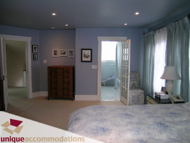Spacious bedroom with blue walls, patterned bedspread, and large windows with curtains. - 1505 Grand Blvd., North Vancouver