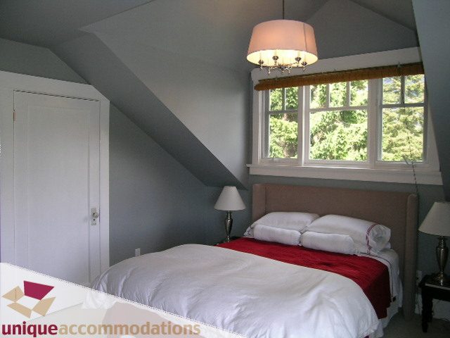Bright bedroom with sloped ceiling, large window, and red throw blanket. - 1505 Grand Blvd., North Vancouver