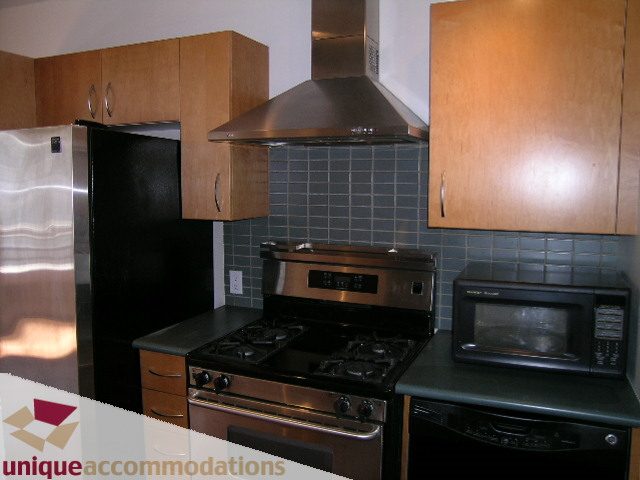 Bright kitchen with stainless steel appliances, black countertops, and wooden cabinets. - 512-1216 Homer Street, Vancouver Downtown