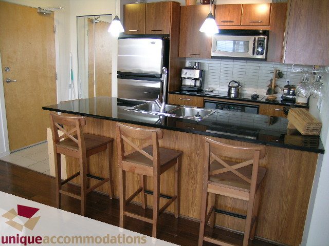 Bright kitchen with black countertops, wooden bar stools, and stainless steel appliances. - 2001-1199 Seymour Street, Vancouver Downtown