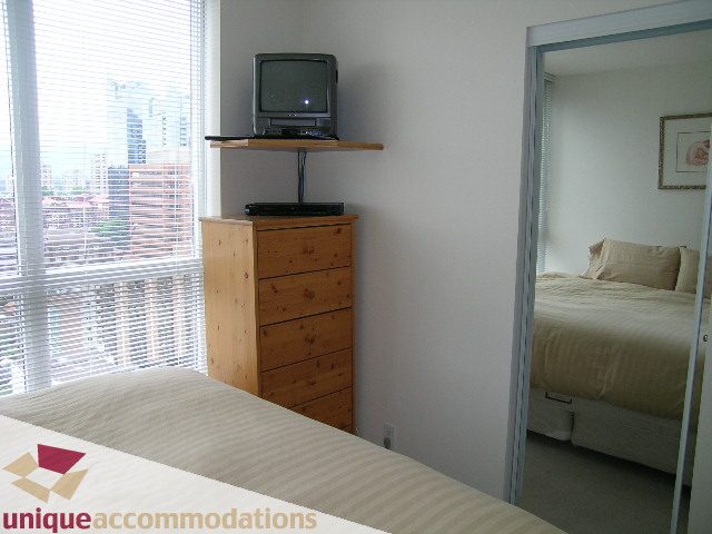 Bright bedroom with city view and wooden dresser, featuring a small TV on a shelf. - 2001-1199 Seymour Street, Vancouver Downtown