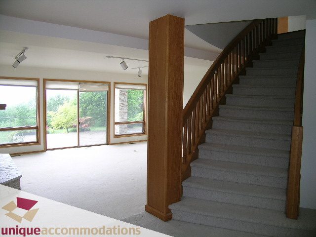 Furnished living room with large windows, hardwood stairs, and a view of greenery outside. - 1472 Camridge Road, West Vancouver