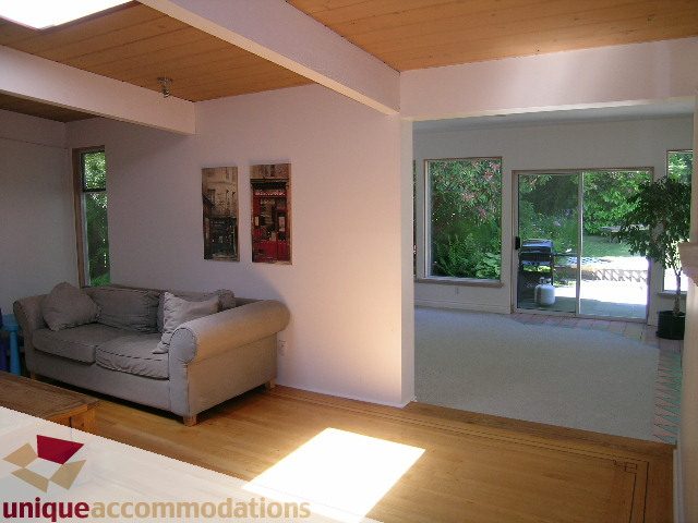 Bright living room with hardwood floors and large windows, showcasing a serene garden view. - 2556 Belloc Street, North Vancouver