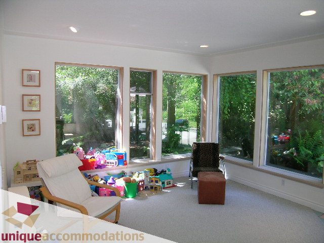 Bright sunroom with large windows, greenery outside, and colorful toys scattered on the floor. - 2556 Belloc Street, North Vancouver