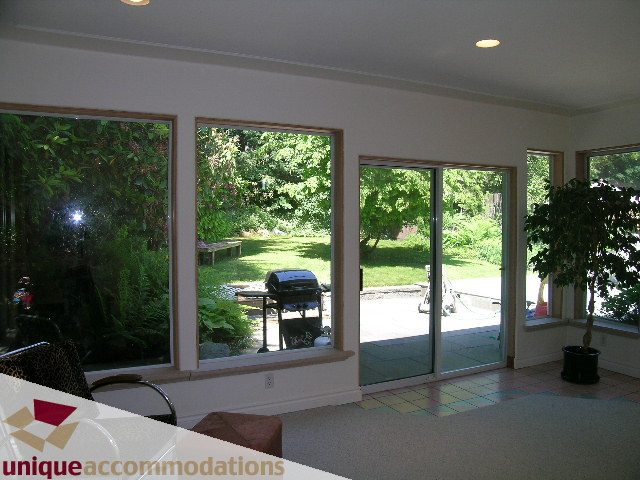 Bright sunroom with large windows overlooking lush greenery, hardwood floors, and a sliding glass door leading to the...