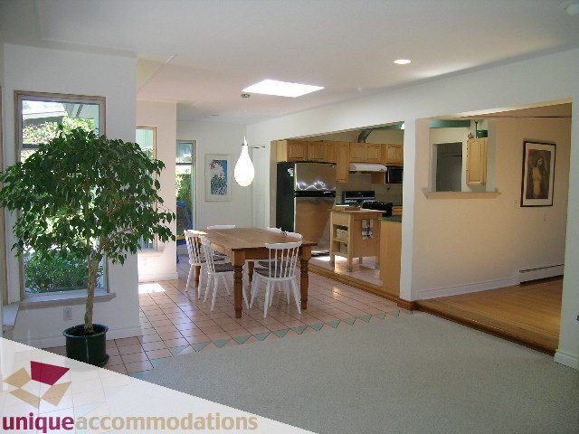 Open-concept living area with hardwood floors and a kitchen in the background. - 2556 Belloc Street, North Vancouver
