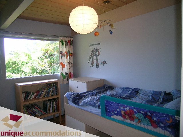 Bright bedroom with twin beds, colorful bedding, and a large window with a view of greenery. - 2556 Belloc Street, North Vancouver