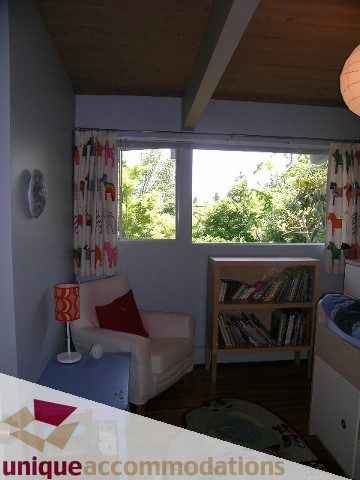Bright living room with large windows, greenery outside, and a cozy reading nook. - 2556 Belloc Street, North Vancouver