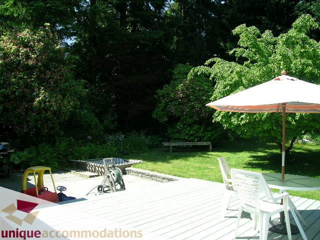 Furnished patio with wooden deck, outdoor furniture, and lush greenery. - 2556 Belloc Street, North Vancouver