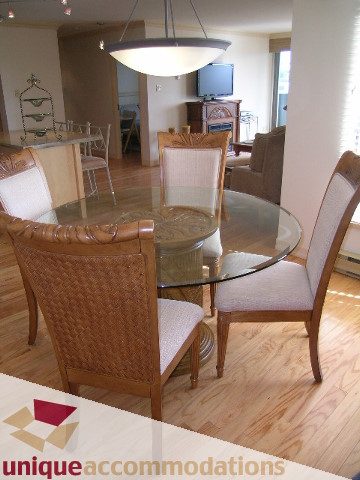 Furnished dining area with glass table, wicker chairs, hardwood floors, and a modern light fixture.