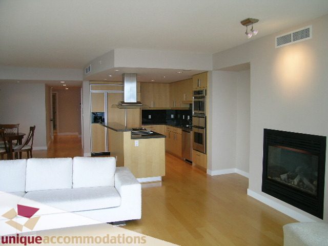 Furnished living room with white couch and fireplace, hardwood floors, and kitchen in background. - 502 - 1233 W. Cordova Street, Vancouver Downtown