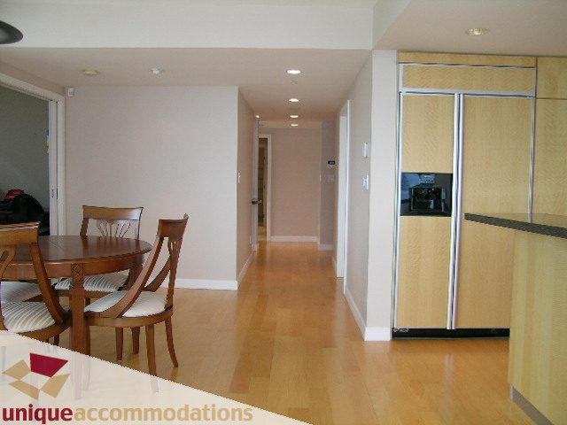 Furnished dining area with wooden table and chairs, hardwood floors, and a modern kitchen in the background.