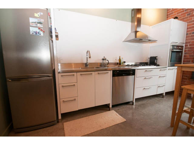 Bright kitchen with stainless steel appliances and white cabinets, featuring a concrete floor and a white rug.