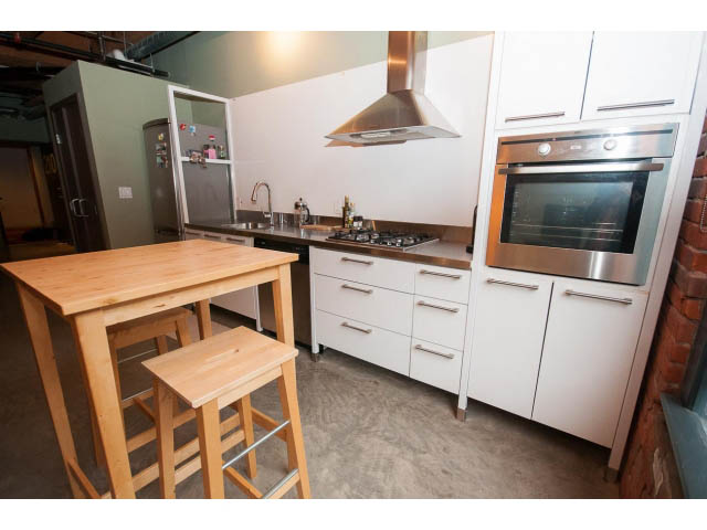 Bright kitchen with white cabinets, stainless steel appliances, and a wooden island. - 210 - 55 E Cordova St, Vancouver Downtown