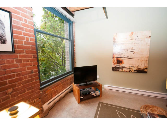 Bright loft with exposed brick walls, large windows, and a cozy corner with a small table and artwork. - 210 - 55 E Cordova St, Vancouver Downtown