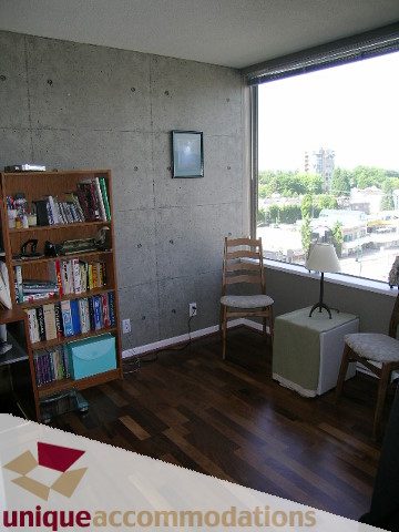 Furnished living room with hardwood floors, city view, and bookshelves. - 802-1590 West 8th Ave, Vancouver West Side