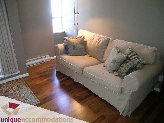 Bright living room with white couch, hardwood floors, and natural light from the window. - 802-1590 West 8th Ave, Vancouver West Side