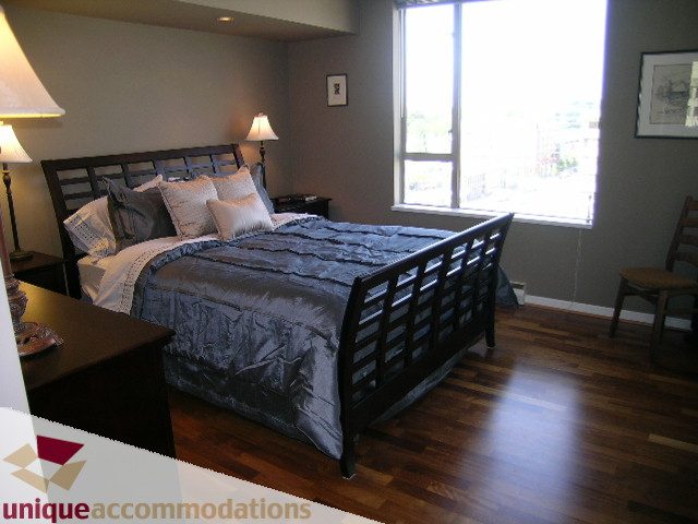 Furnished bedroom with hardwood floors and a large window, showcasing a city view. - 802-1590 West 8th Ave, Vancouver West Side