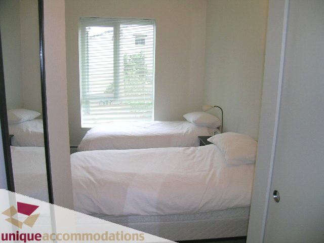 Bright bedroom with two twin beds and a window with blinds. - 184 Chesterfield Avenue, North Vancouver