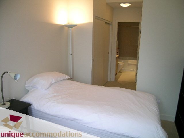 Bright bedroom with white bedding and a tall floor lamp, leading to a hallway. - 184 Chesterfield Avenue, North Vancouver