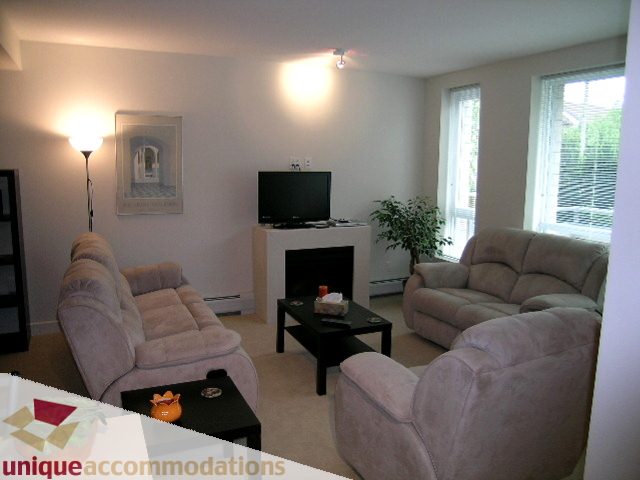 Furnished living room with beige couches, coffee table, and wall-mounted TV. - 184 Chesterfield Avenue, North Vancouver