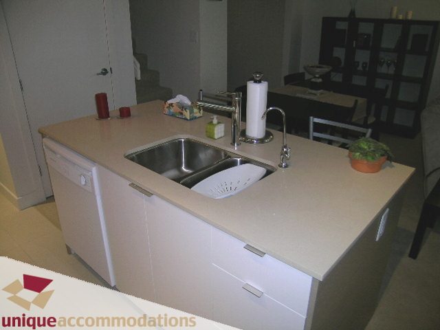 Bright kitchen with white countertops and modern sink, featuring a dining area in the background. - 184 Chesterfield Avenue, North Vancouver