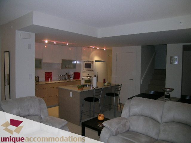 Furnished living room with beige couch and kitchen in the background. - 184 Chesterfield Avenue, North Vancouver