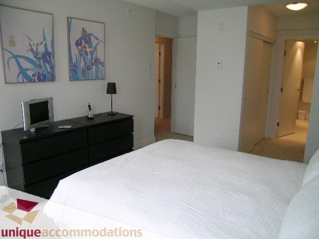 Furnished bedroom with white bedding and black dresser, featuring floral artwork on the wall. - 184 Chesterfield Avenue, North Vancouver