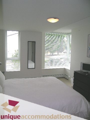 Bright bedroom with large windows, white bedding, and a dresser. - 184 Chesterfield Avenue, North Vancouver