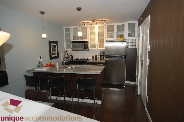 Modern kitchen with dark wood cabinets, stainless steel appliances, and a dining area with black chairs. - 1229 Richards Street, Vancouver Downtown