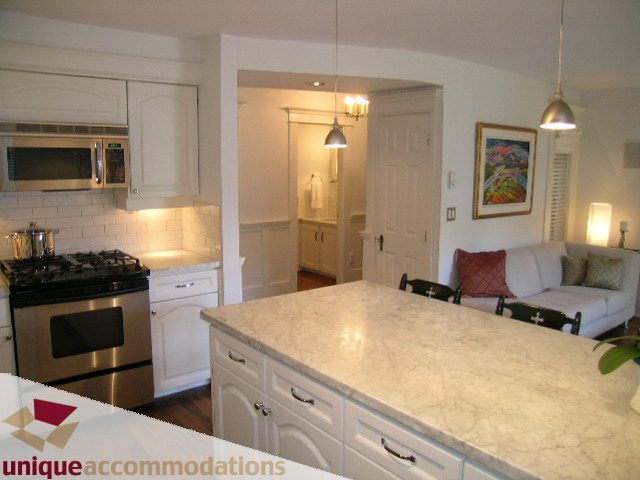 Bright kitchen with white cabinetry and granite countertops, leading to a cozy living area with a couch and artwork.