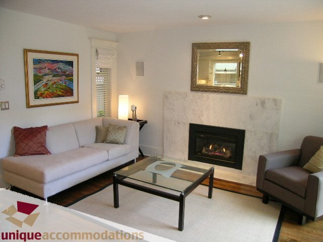 Living room with modern furniture, glass coffee table, marble fireplace, and framed artwork. - 1815 Creelman Avenue, Vancouver West Side