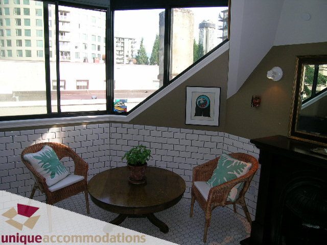 Furnished living room with city view, wicker furniture, and brick accent wall. - 995 Bute Street "Rand House", Vancouver Downtown