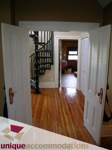 Bright hallway leading to spiral staircase, hardwood floors, open door revealing another room. - 995 Bute Street "Rand House", Vancouver Downtown