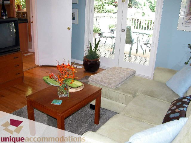 Furnished living room with hardwood floors, a cozy sofa, and a wooden coffee table adorned with flowers. - 1872 Greenock Place, North Vancouver