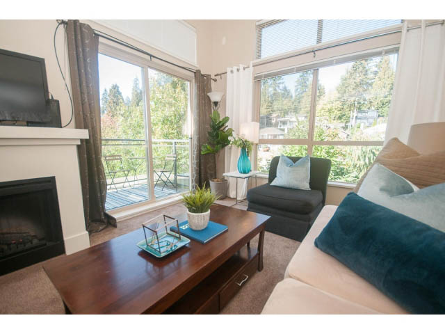 Bright living room with large windows, city view, and cozy furnishings. - 418 - 1633 Mackay Avenue, North Vancouver