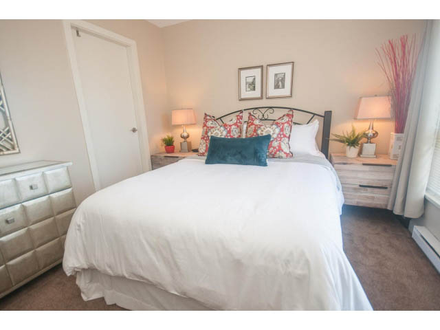 Furnished 2-bedroom bedroom with white bedding, teal accents, and a cozy ambiance. - 418 - 1633 Mackay Avenue, North Vancouver